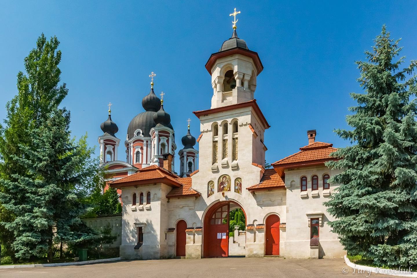 Orthodox monastery with distinctive white-and-red facade, golden domes, and crosses in clear daylight