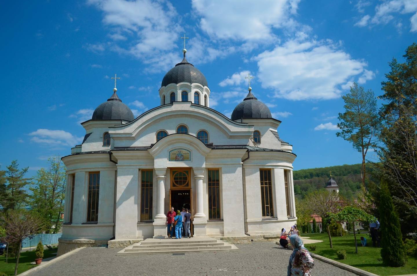 Orthodox monastery with white facade, golden domes, and manicured grounds under blue sky