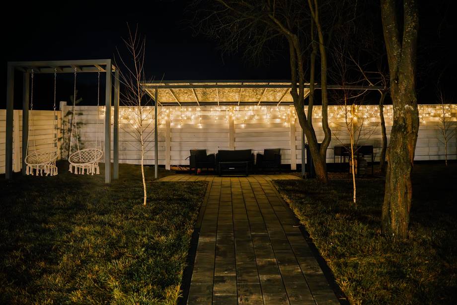 Evening terrace with modern pergola and ambient lighting, paved pathway approach
