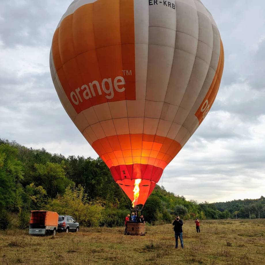 Hot air balloon with orange branding preparing for flight in a rural field with support crew