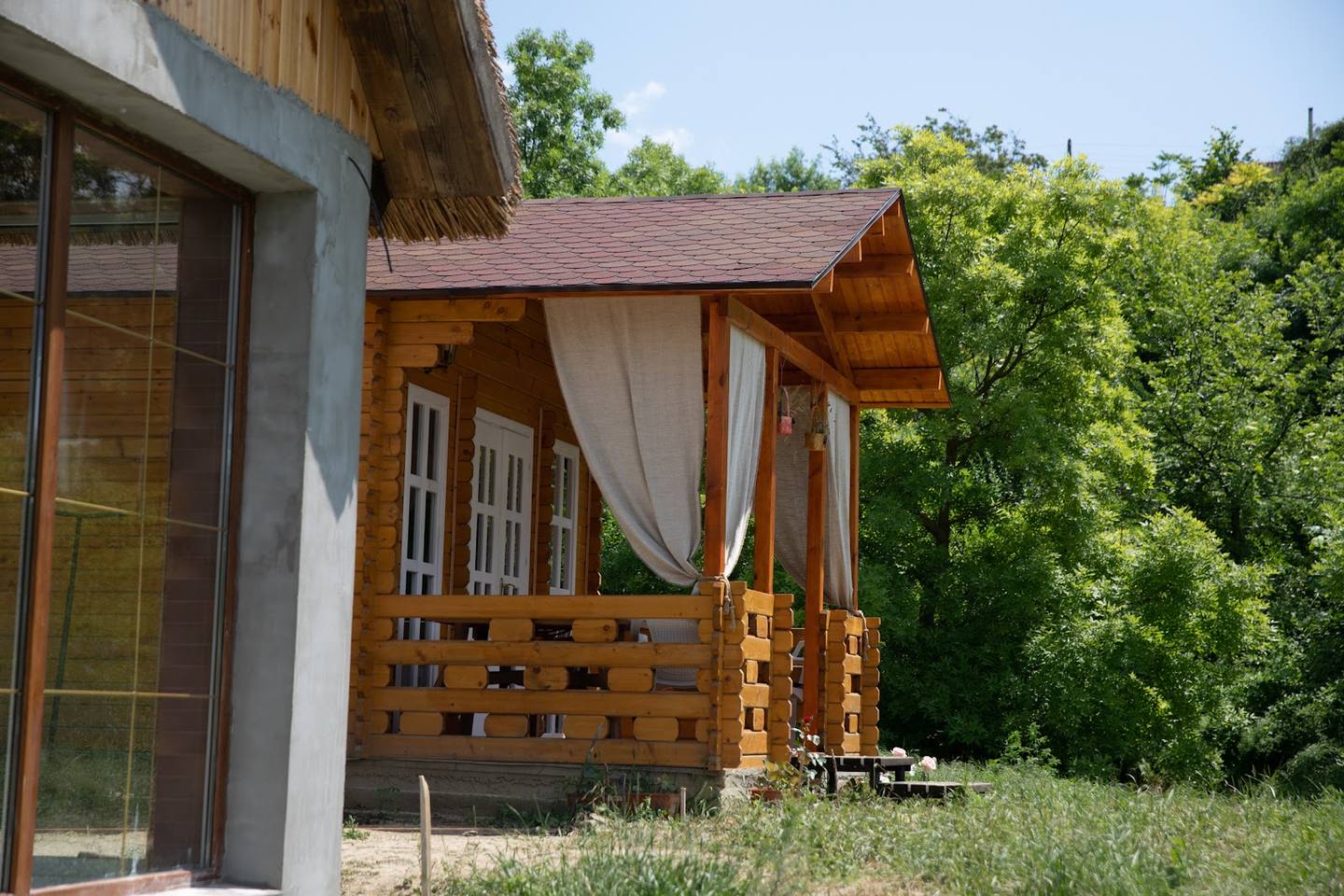 Rustic outdoor wooden pavilion with white fabric drapes and modern glass entrance