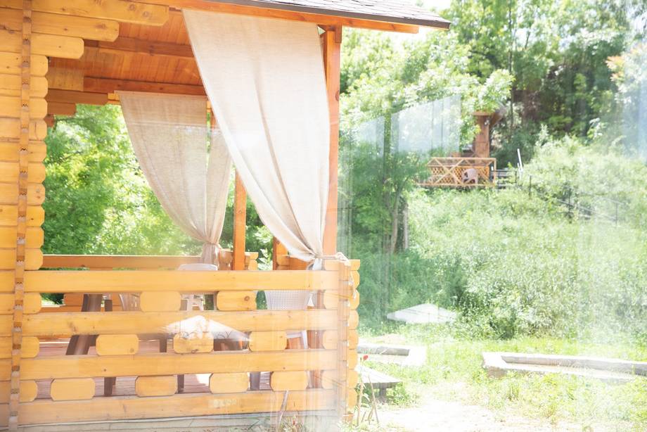 Wooden terrace pavilion with white curtains overlooking green countryside