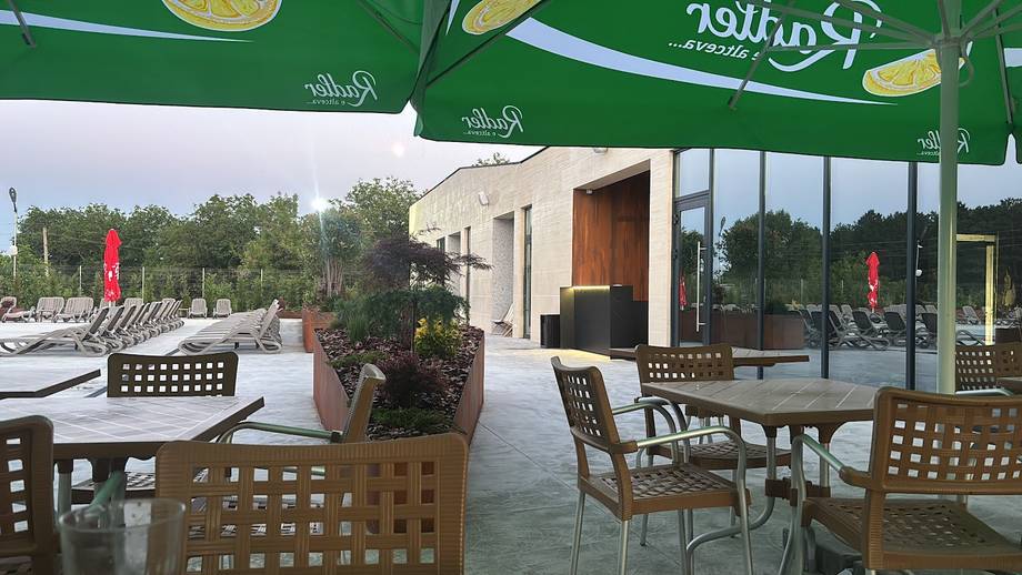 Outdoor terrace with green umbrellas, wooden furniture, and modern glass-enclosed dining space