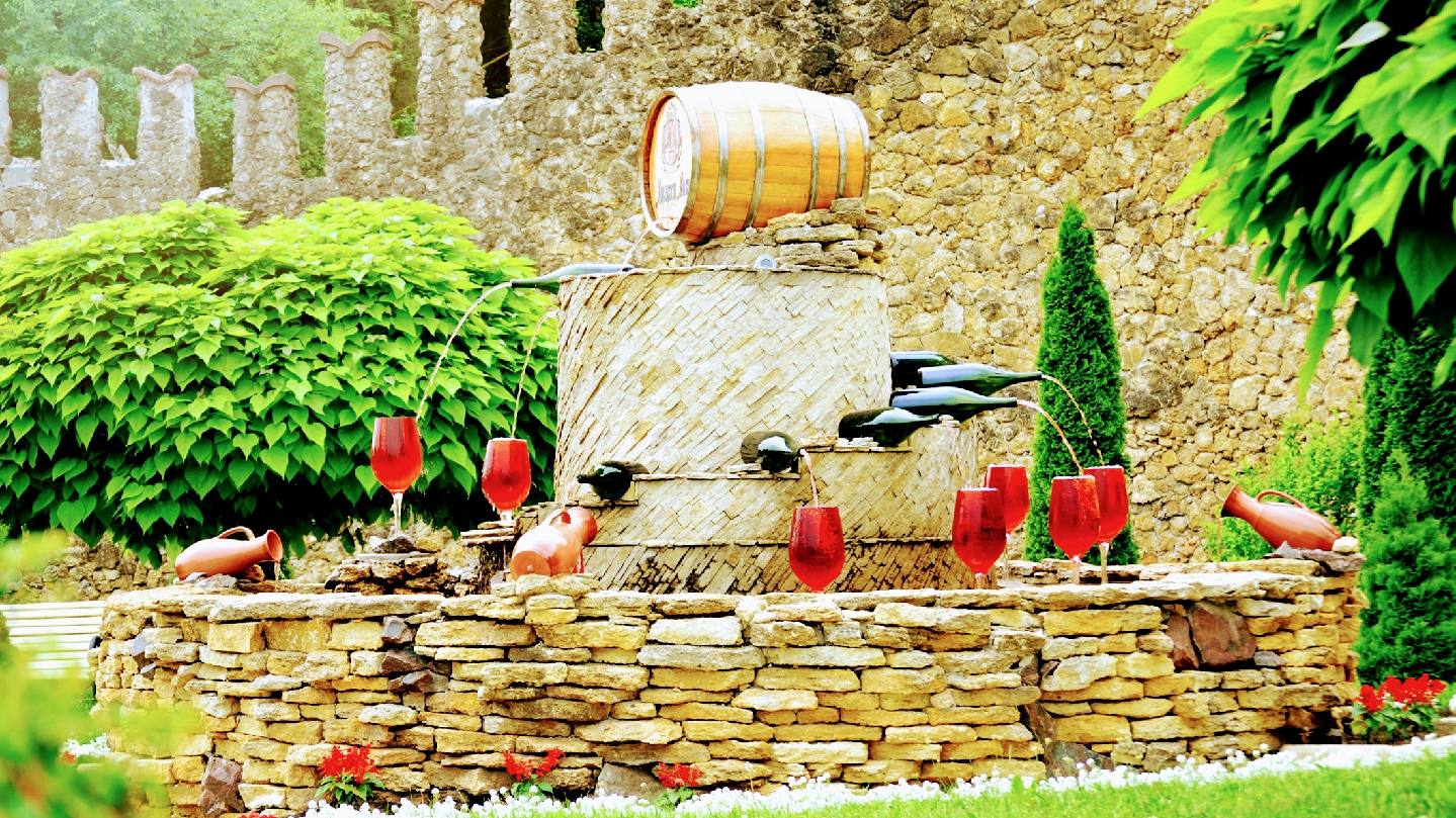 Rustic vineyard setting with wooden barrel and red wine bottles on stone wall