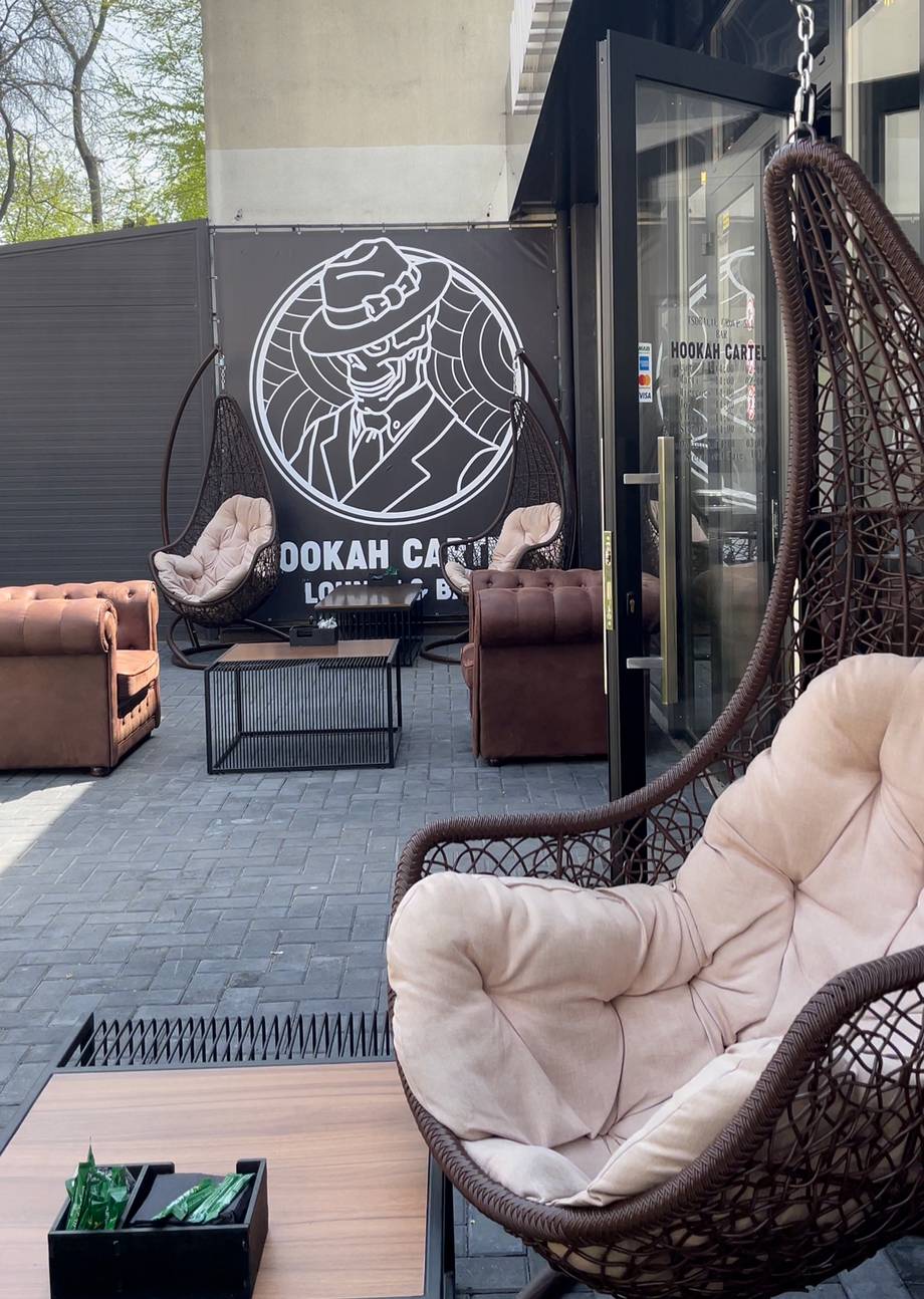 Outdoor terrace with neon hookah lounge sign, hanging chairs, and lounge seating