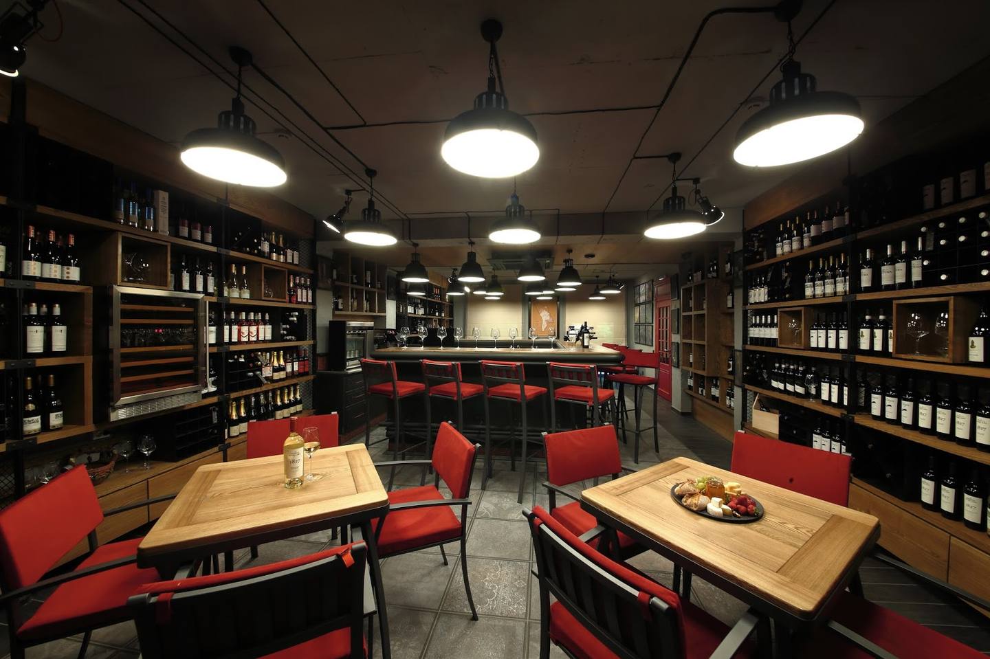 Wine bar interior with floor-to-ceiling bottle displays, wooden tables, and red seating