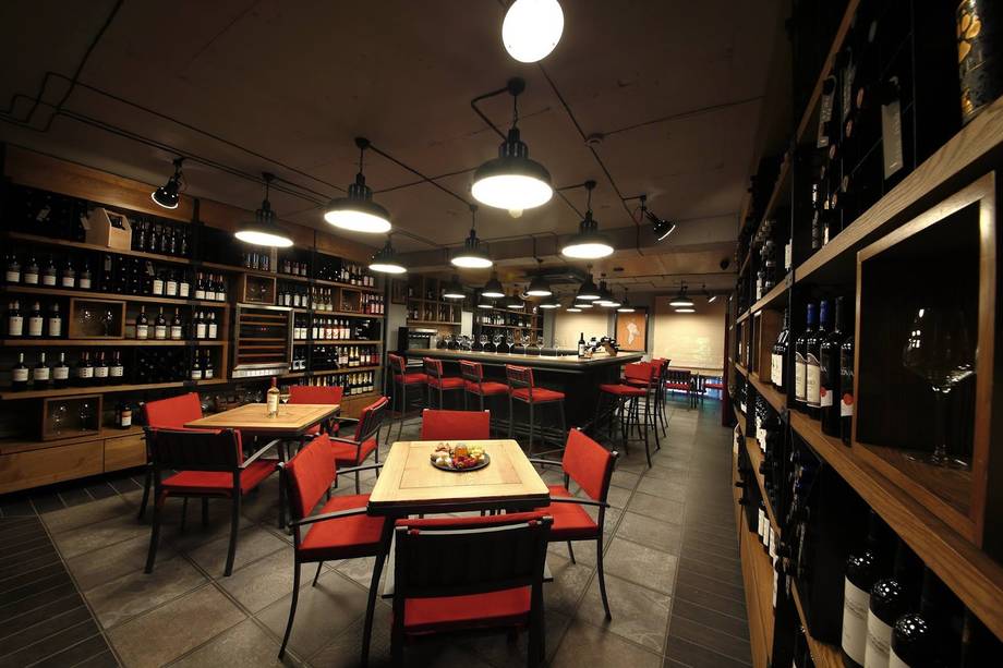 Wine bar interior with floor-to-ceiling bottle displays, red seating, and warm ambient lighting