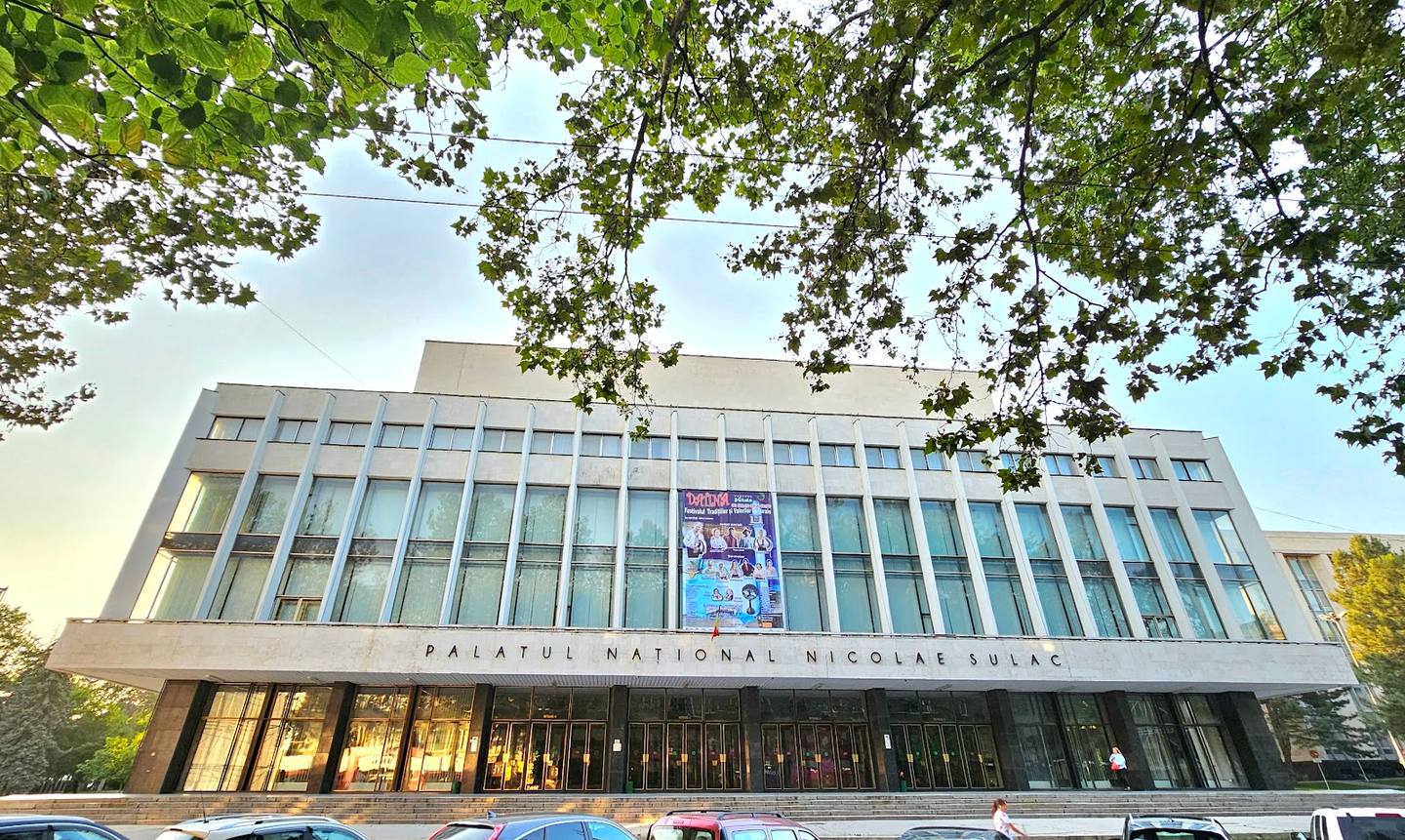 Modern institutional building facade with distinctive vertical striping and ground-level colonnade entrance
