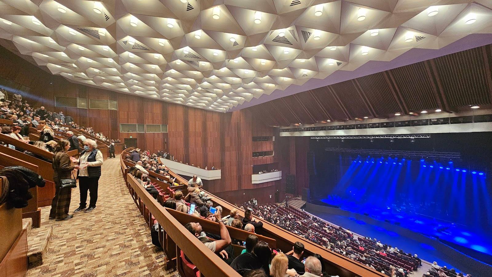Concert hall interior with tiered seating and blue stage lighting during performance