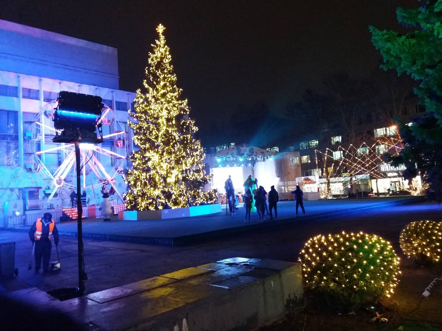 Festive outdoor plaza with illuminated Christmas tree and holiday lighting at night