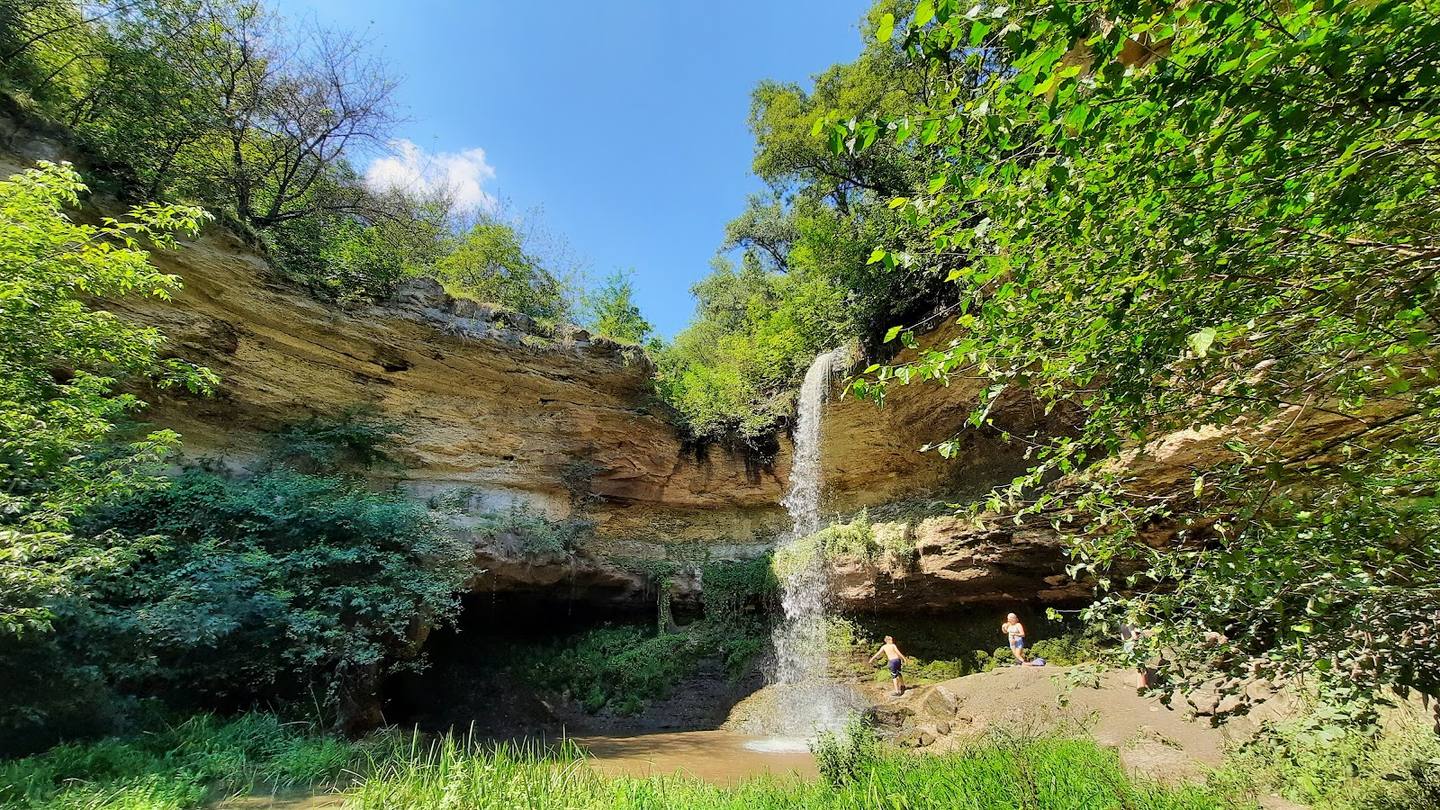 Waterfall cascades through lush forest gorge with moss-covered limestone cliffs