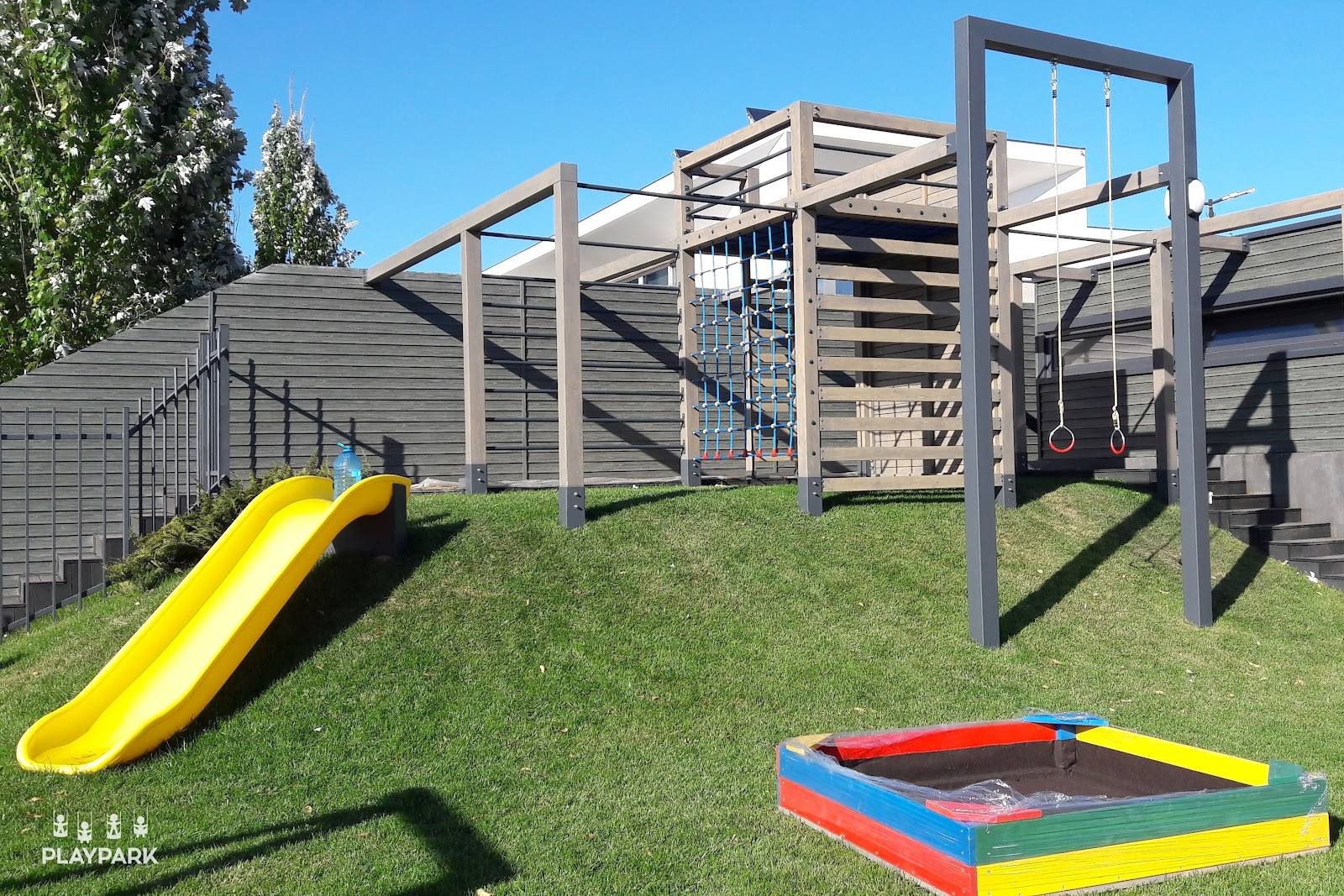 Outdoor playground with climbing structure, slide, and trampoline in manicured garden setting