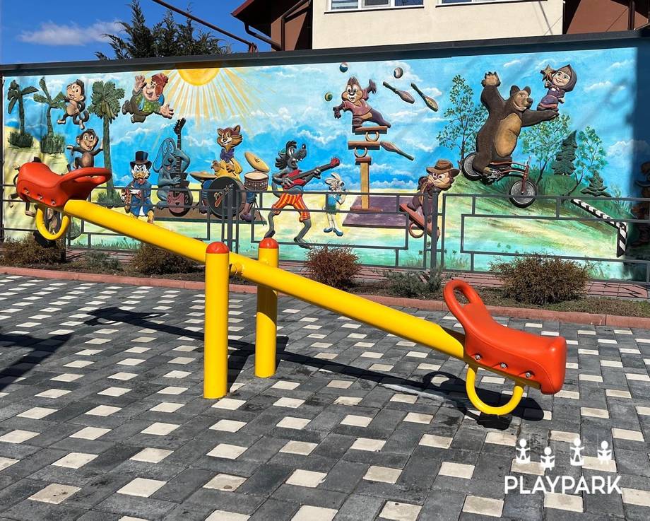 Bright yellow seesaw and red ride-on toy on patterned ground with colorful mural backdrop at PLAYPARK