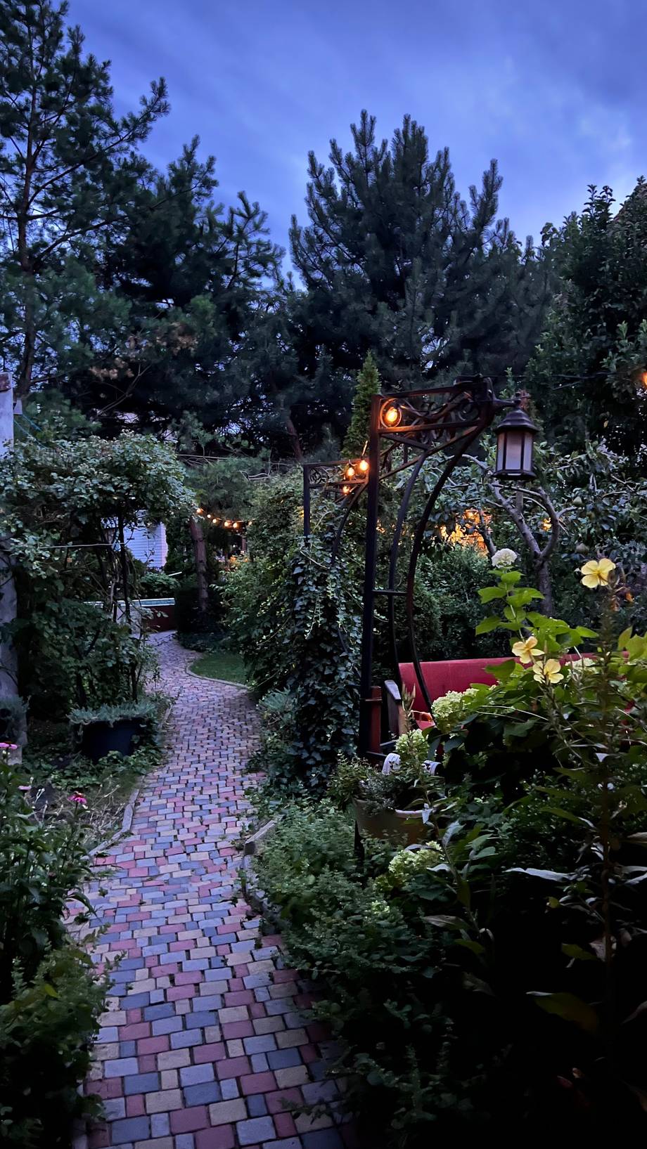 Lush garden terrace with lit archway at twilight, brick pathway leading through landscaped seating area