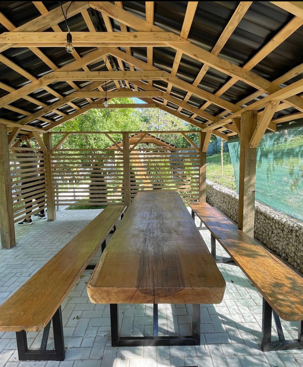 Wooden pergola terrace with long dining table and benches overlooking garden
