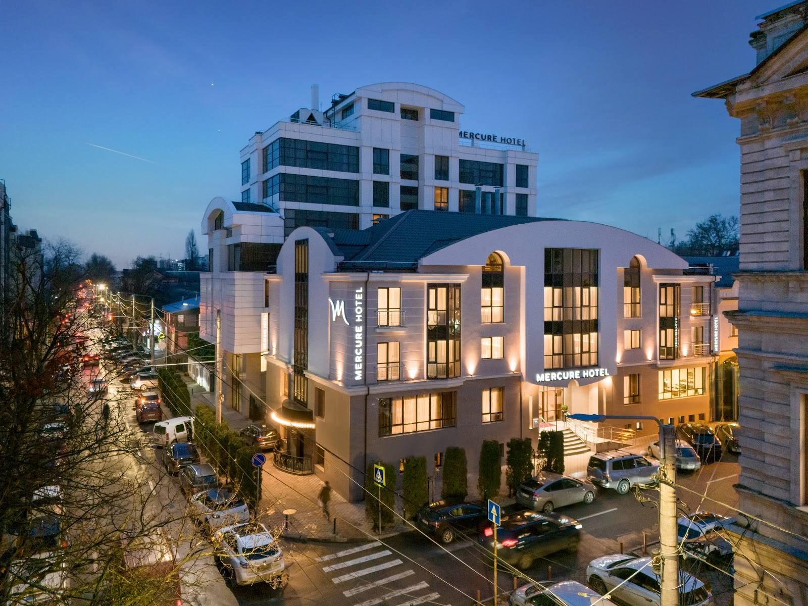 Modern hotel building with illuminated facade at dusk, mixed-use development with residential and commercial spaces