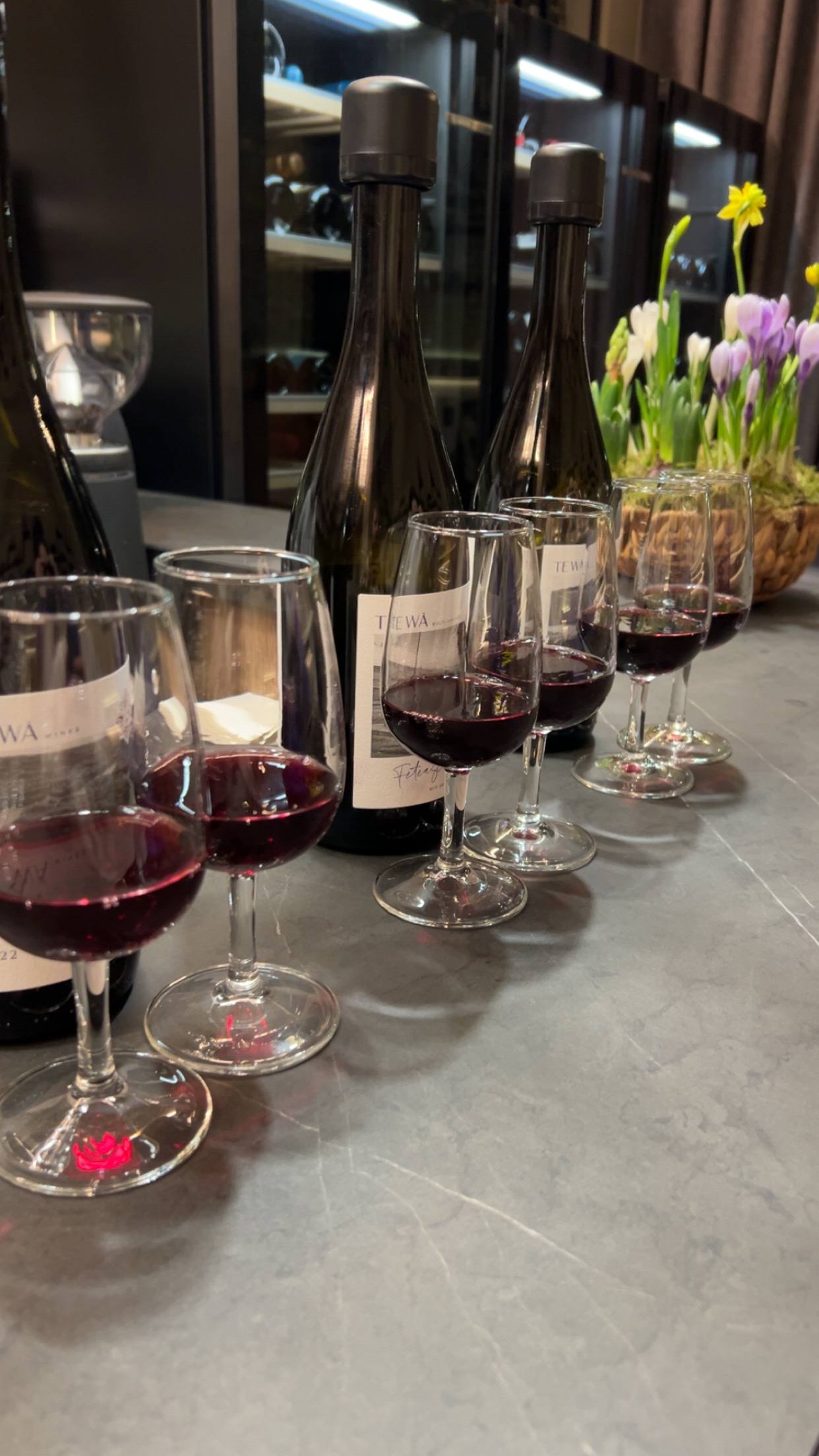 Wine tasting setup with red wine pours and fresh flowers on service counter