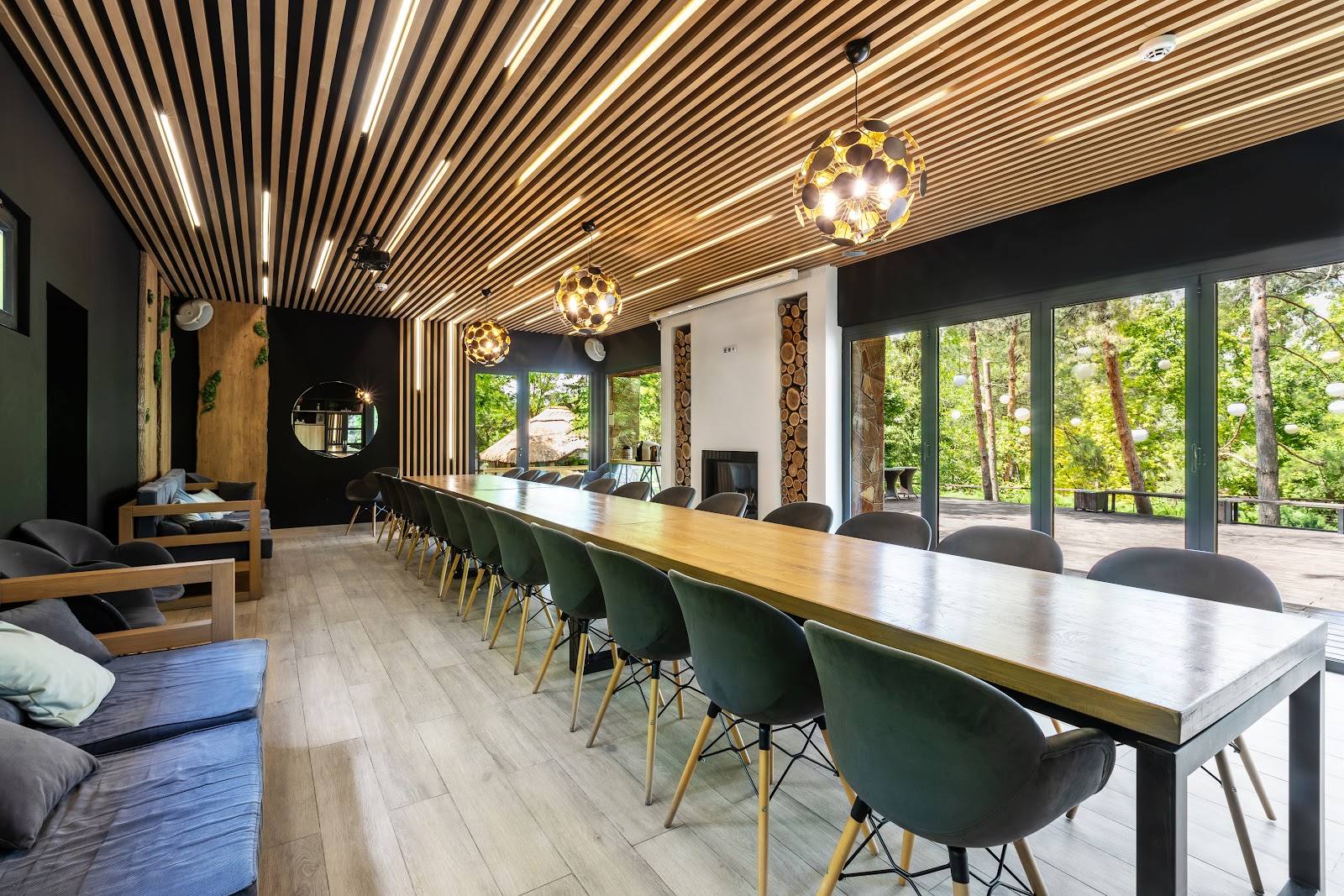 Modern event space with long dining table, geometric ceiling, floor-to-ceiling windows overlooking gardens