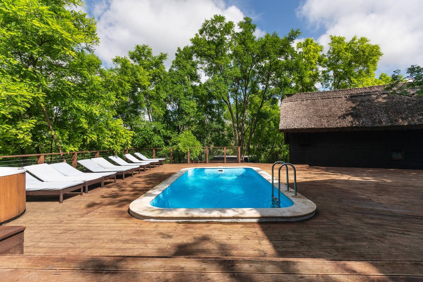 Outdoor terrace with swimming pool, wooden deck, and lounge seating surrounded by trees