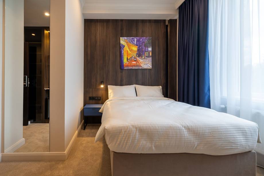 Modern hotel room with white bedding, contemporary furnishings, and natural light from floor-to-ceiling window