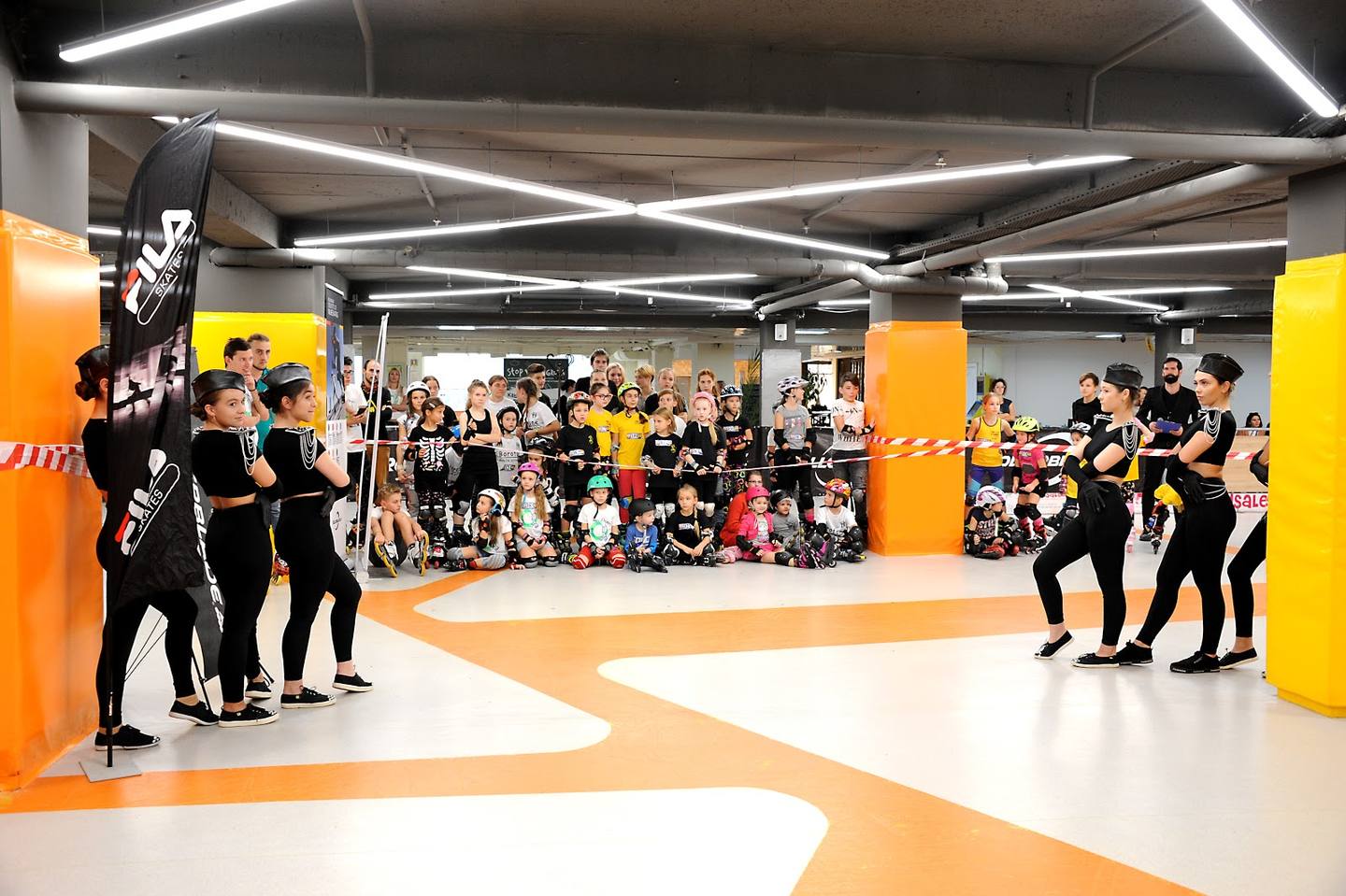 Skateboarding or action sports arena with bold yellow and orange columns, polished floor and spectators
