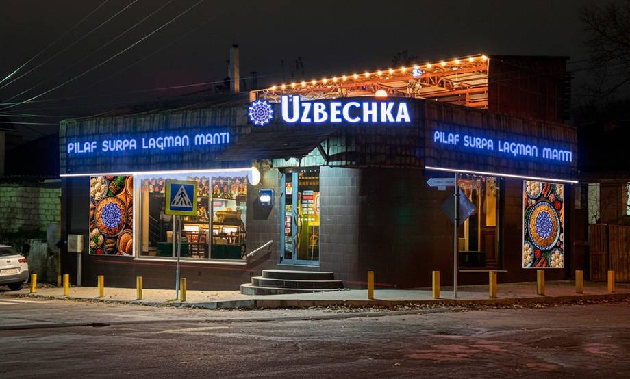 Uzbekchka restaurant storefront at night with illuminated signage and outdoor seating