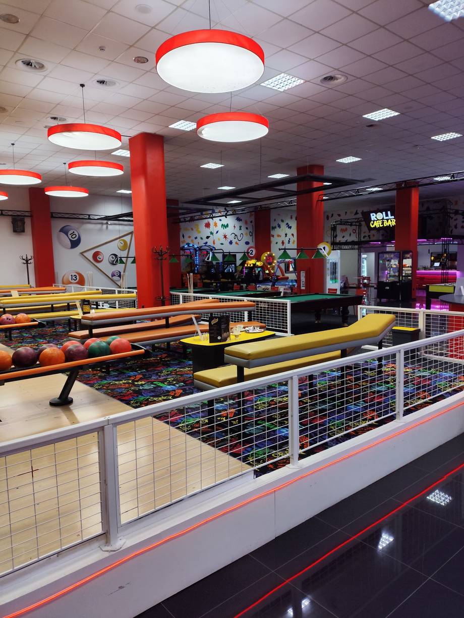 Indoor mini-golf course with red ceiling lights and white safety barriers