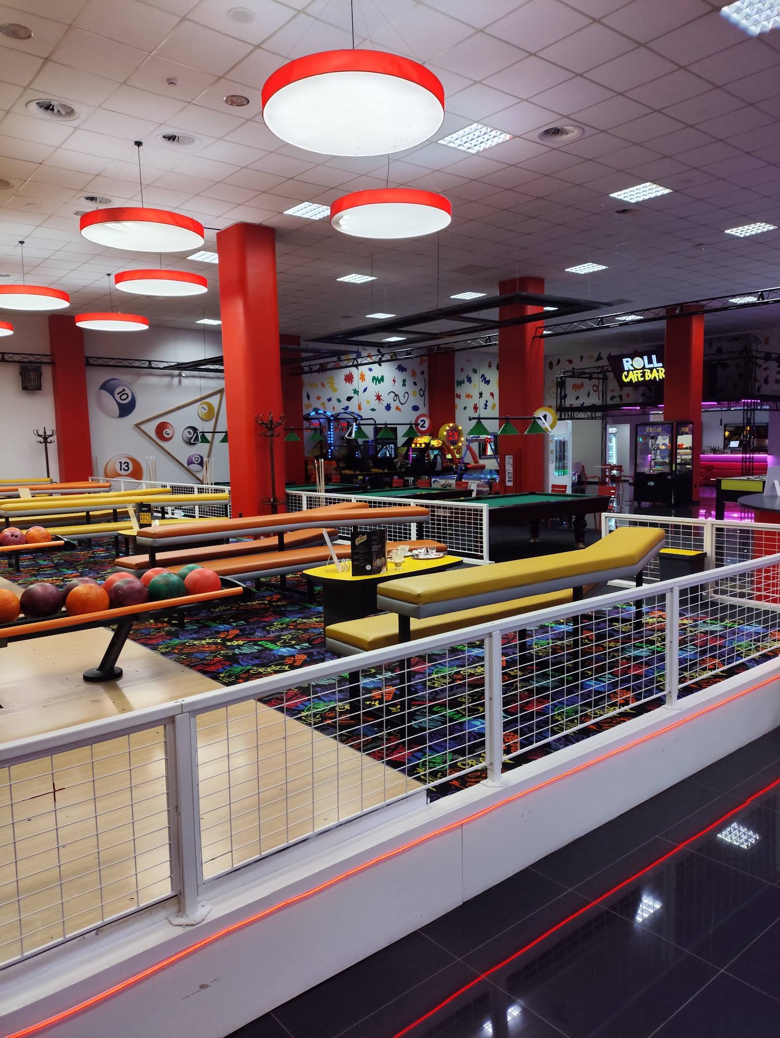 Indoor mini-golf course with red ceiling lights and white safety barriers