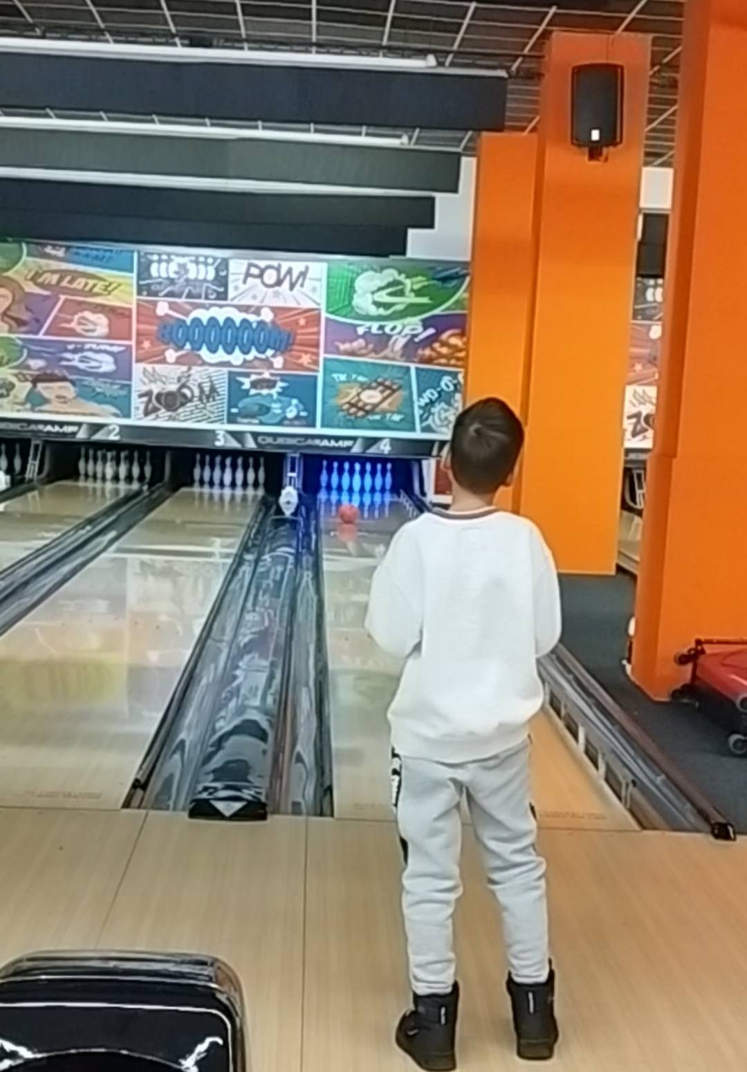 Bowling alley lane with player in action, bright orange structural elements visible
