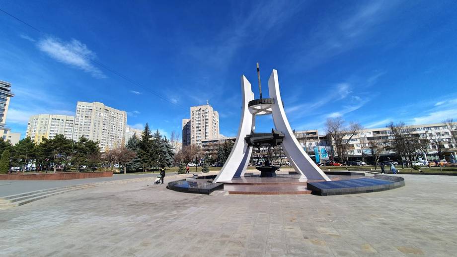 Outdoor public square with modern monument and cityscape backdrop