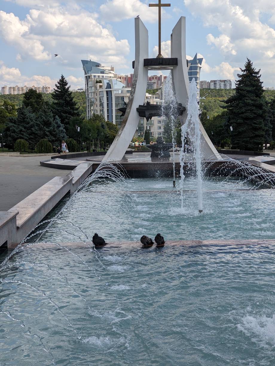 Monumental fountain and memorial complex with distinctive white architecture and cross in urban park setting