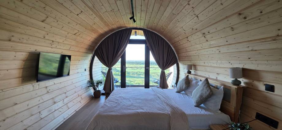 Modern glamping pod interior with round window overlooking rural landscape