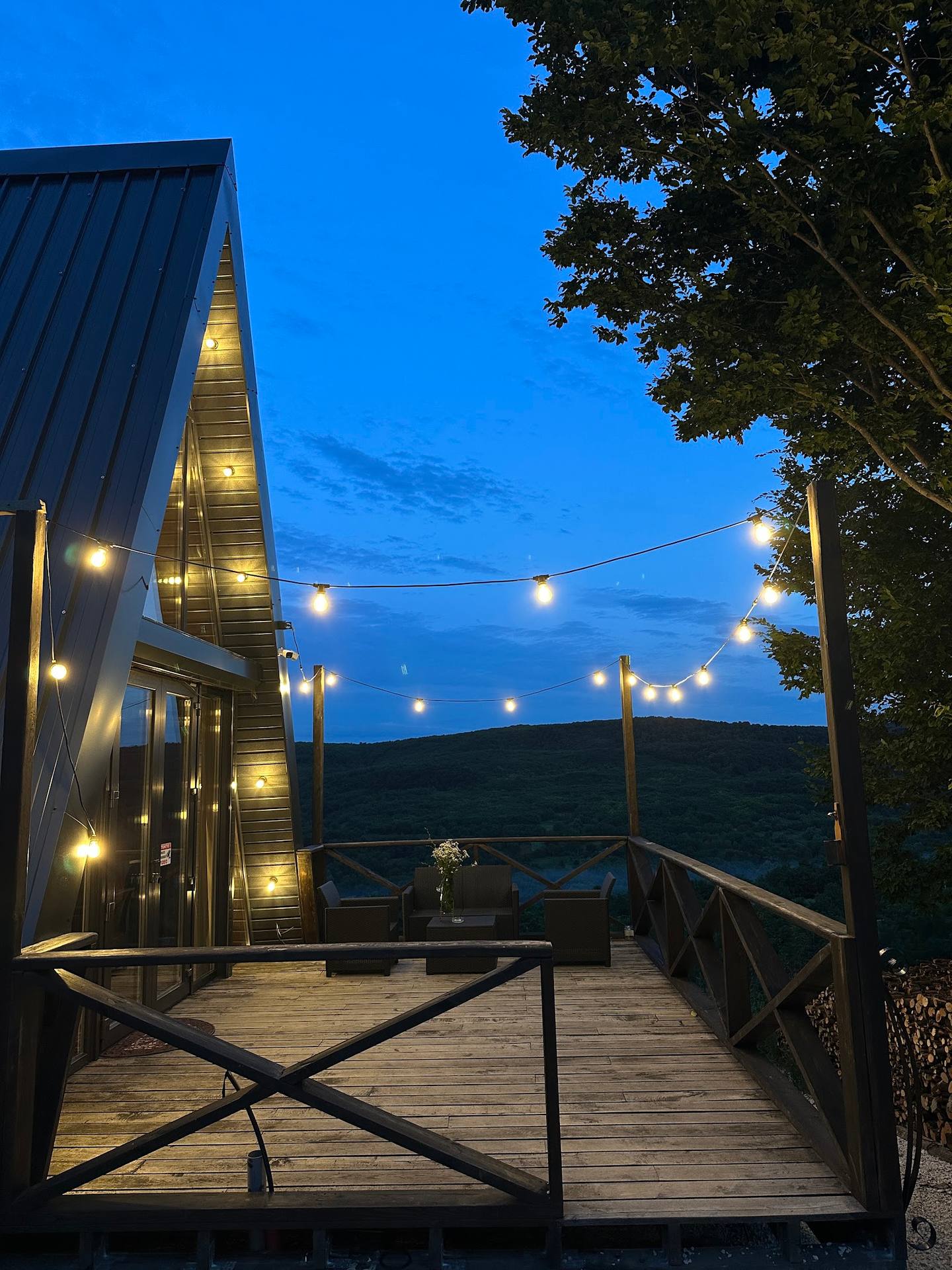 Modern wooden terrace pavilion at dusk with string lights and mountain views