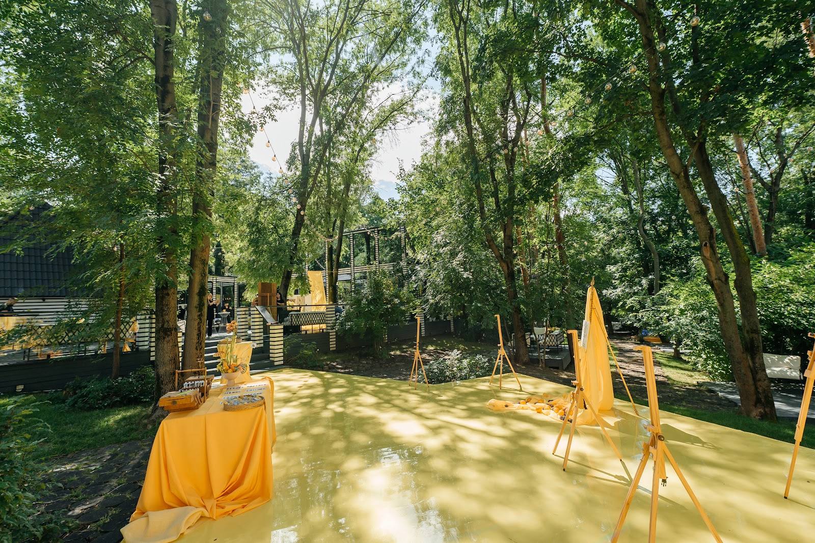 Wedding ceremony aisle setup under mature trees with yellow fabric draping and archway