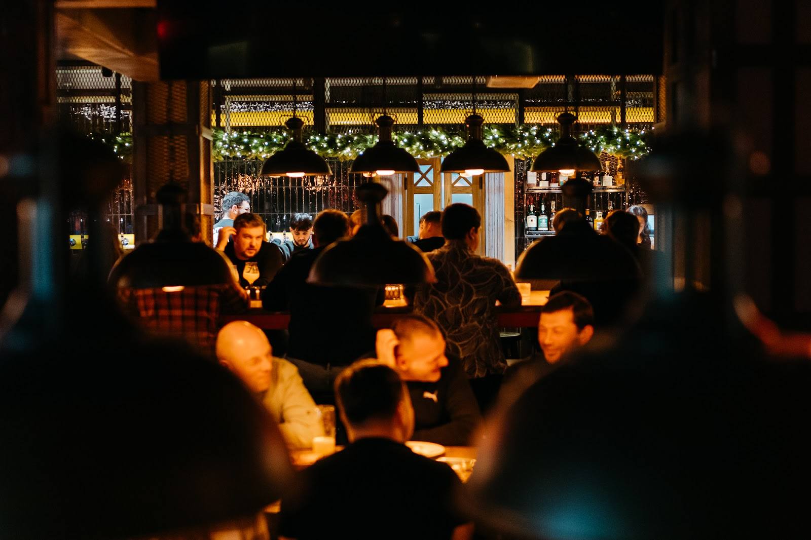 Crowded bar interior with warm amber lighting and decorated back wall during evening service