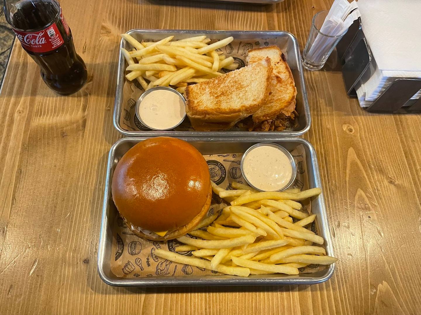 Two meal trays with burgers, fries, and sauces on wooden table