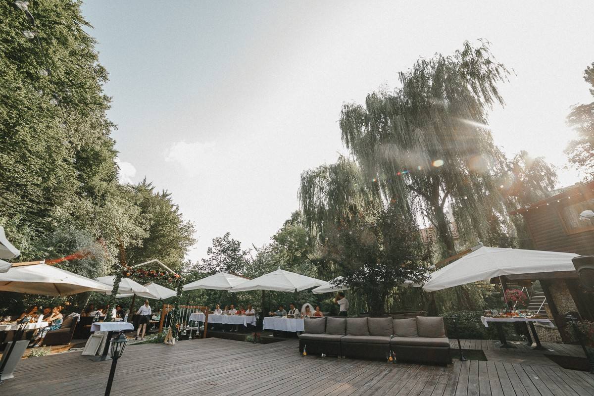 Outdoor terrace with white umbrellas and wooden deck beneath mature weeping willow trees