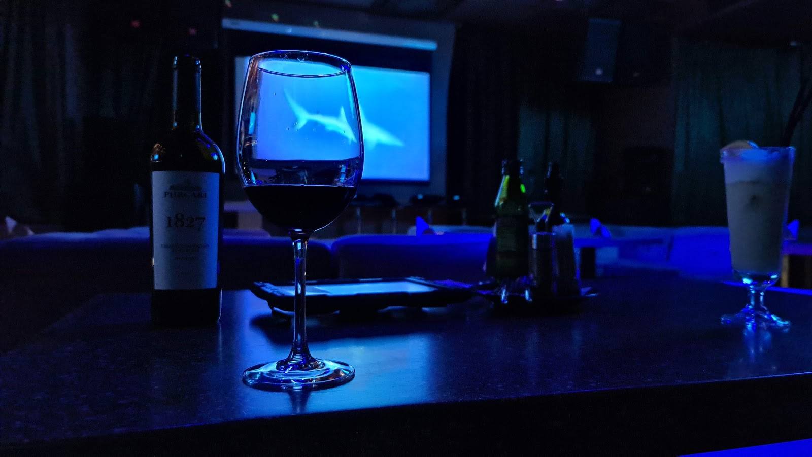Bar counter with blue ambient lighting, screen display, and wine bottles