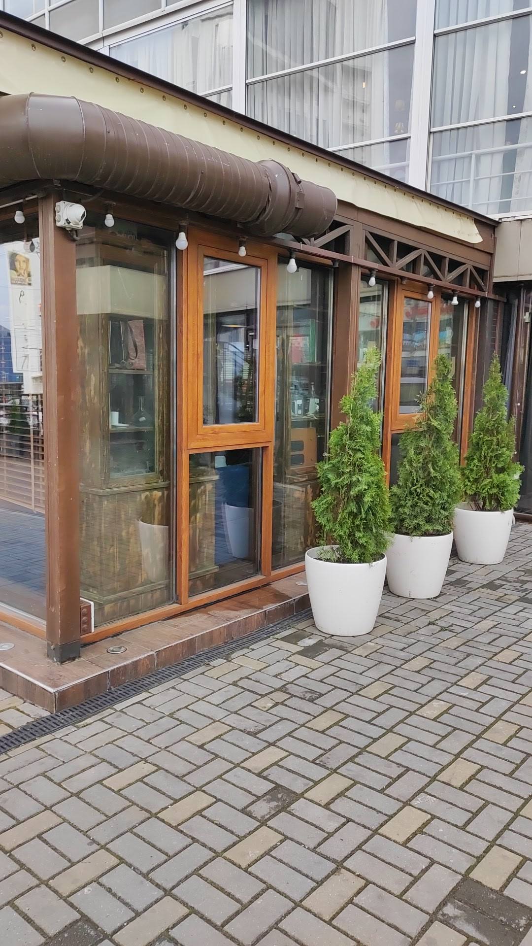 Restaurant storefront with wooden frame windows and planted entrance on brick paving
