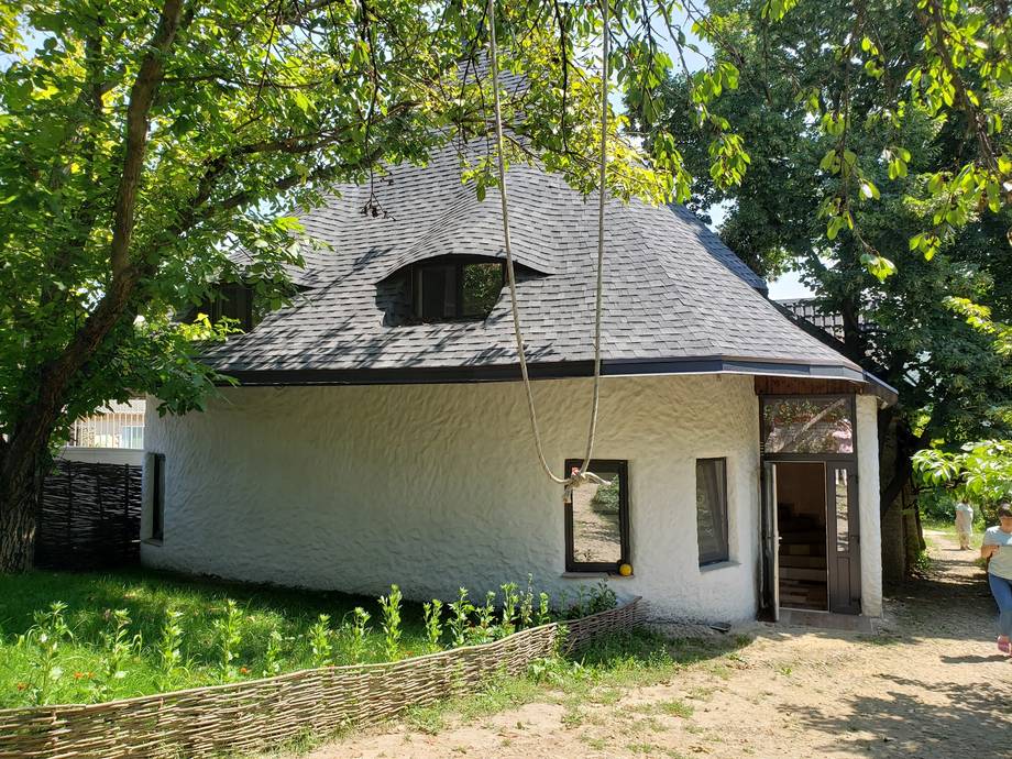 Distinctive round white-walled building with charcoal roof surrounded by mature trees