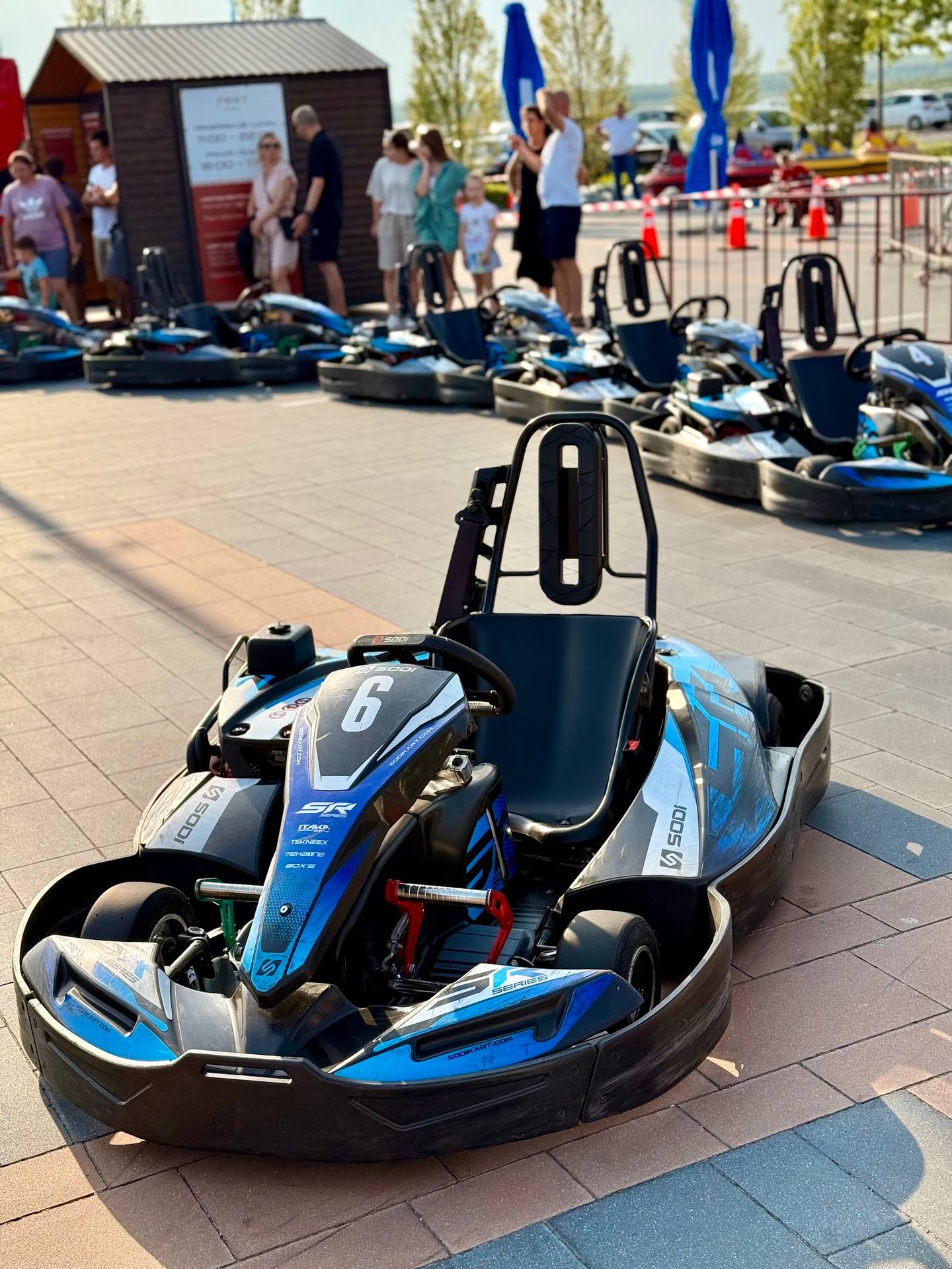 Blue and black go-kart in foreground with track and waiting riders in background