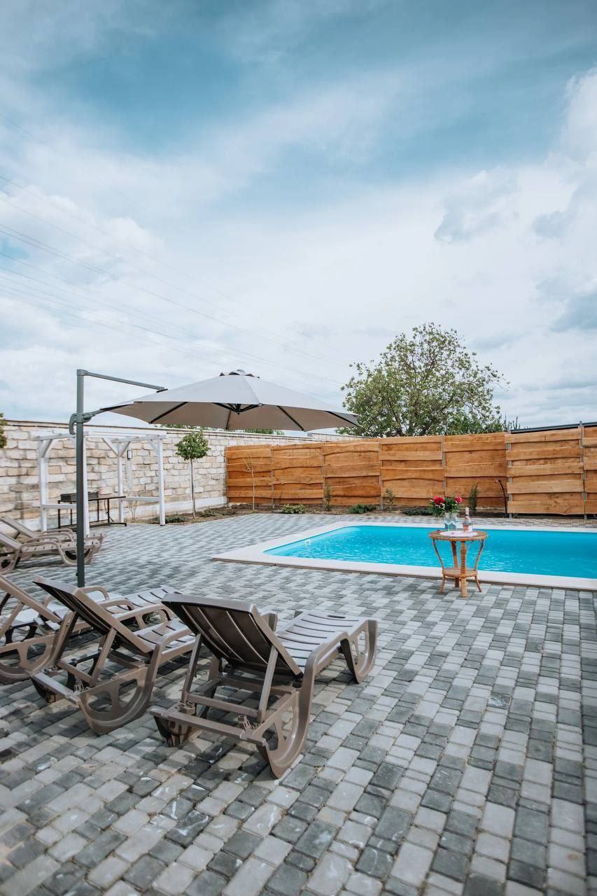 Pool terrace with lounge chairs, wooden fence, and blue swimming pool under open sky