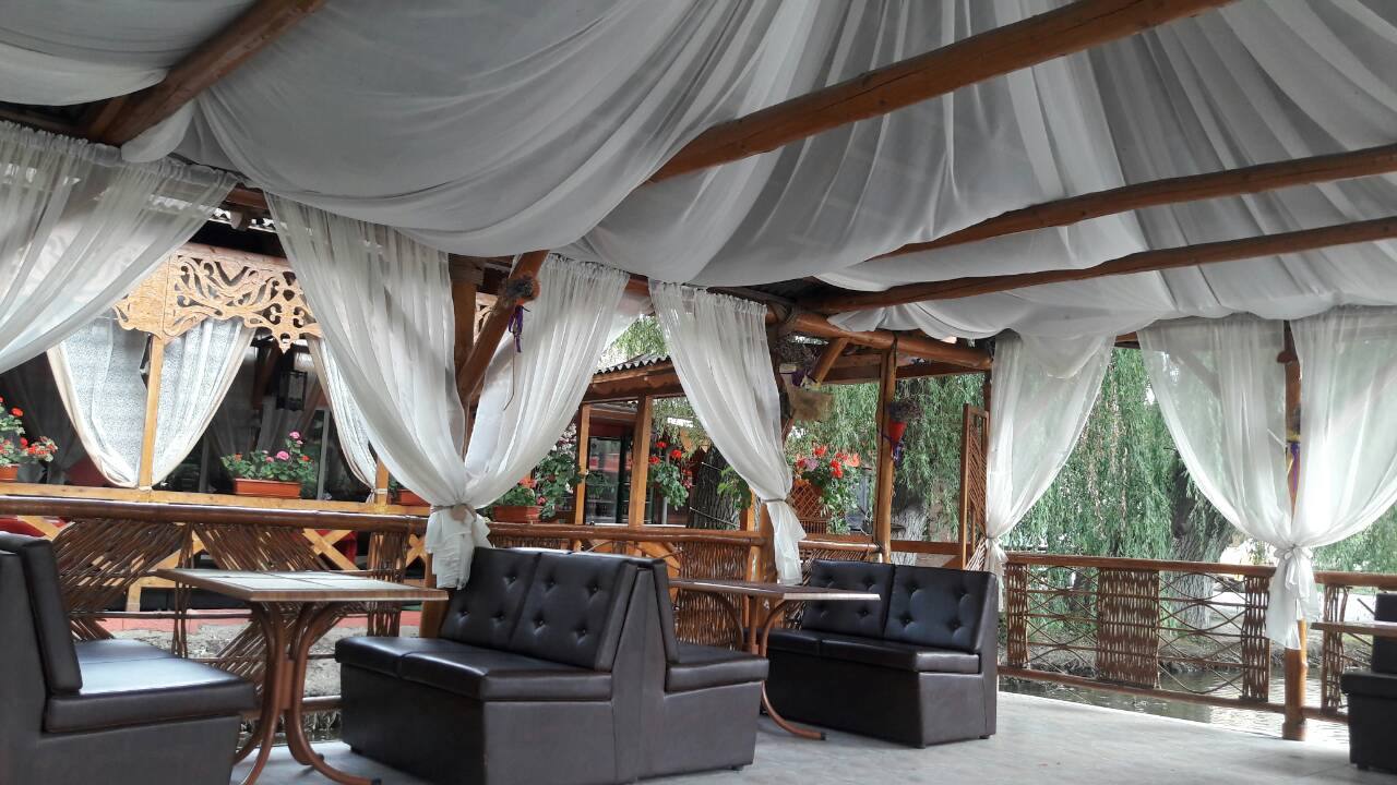 Spacious tent interior with draped white fabric, wooden beams, and black seating areas for event hosting