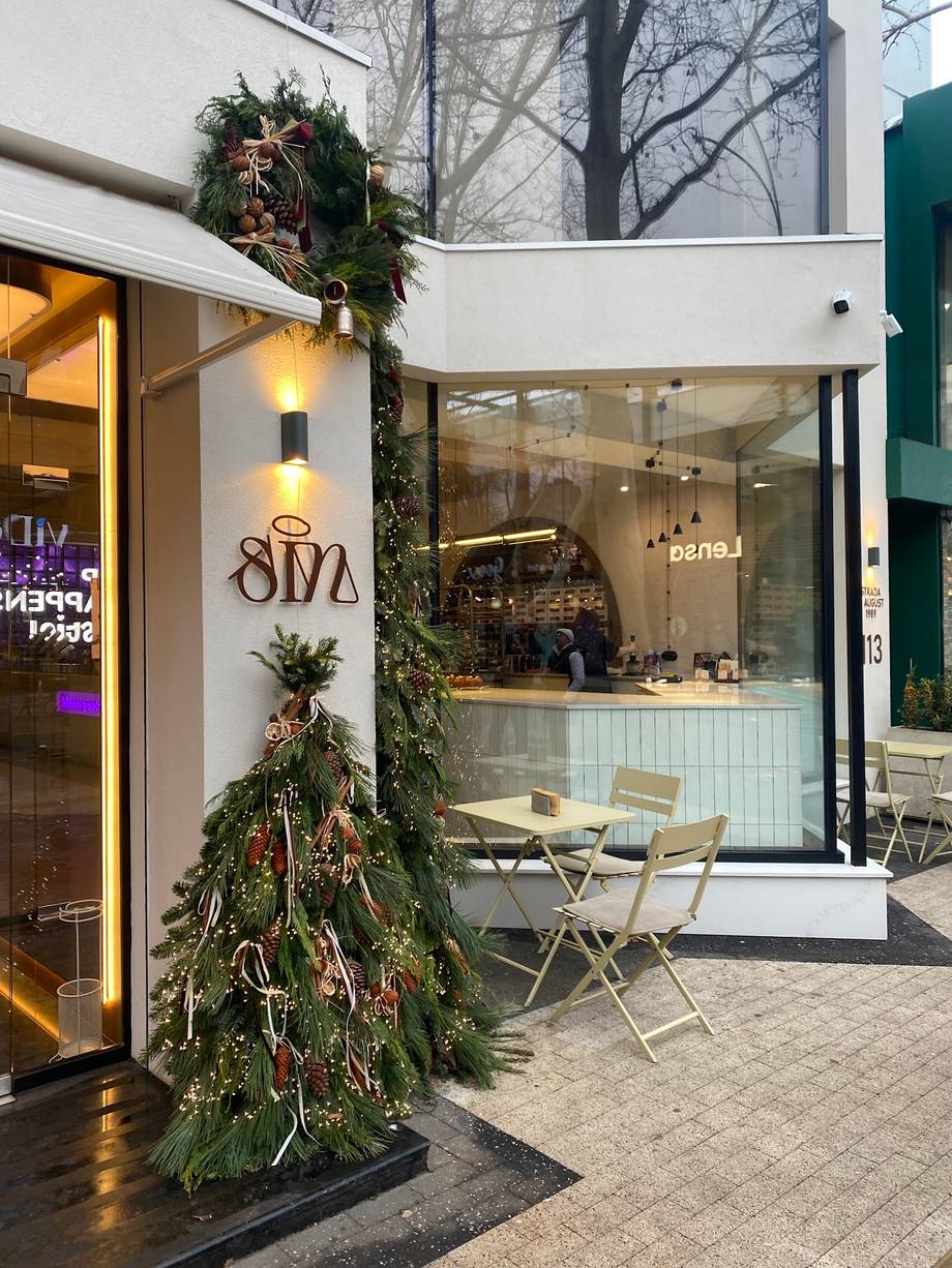 Modern storefront with white facade, large windows, and festive holiday greenery display