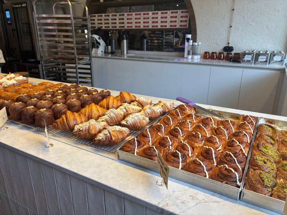 Bakery display case with fresh croissants and pastries under counter lighting