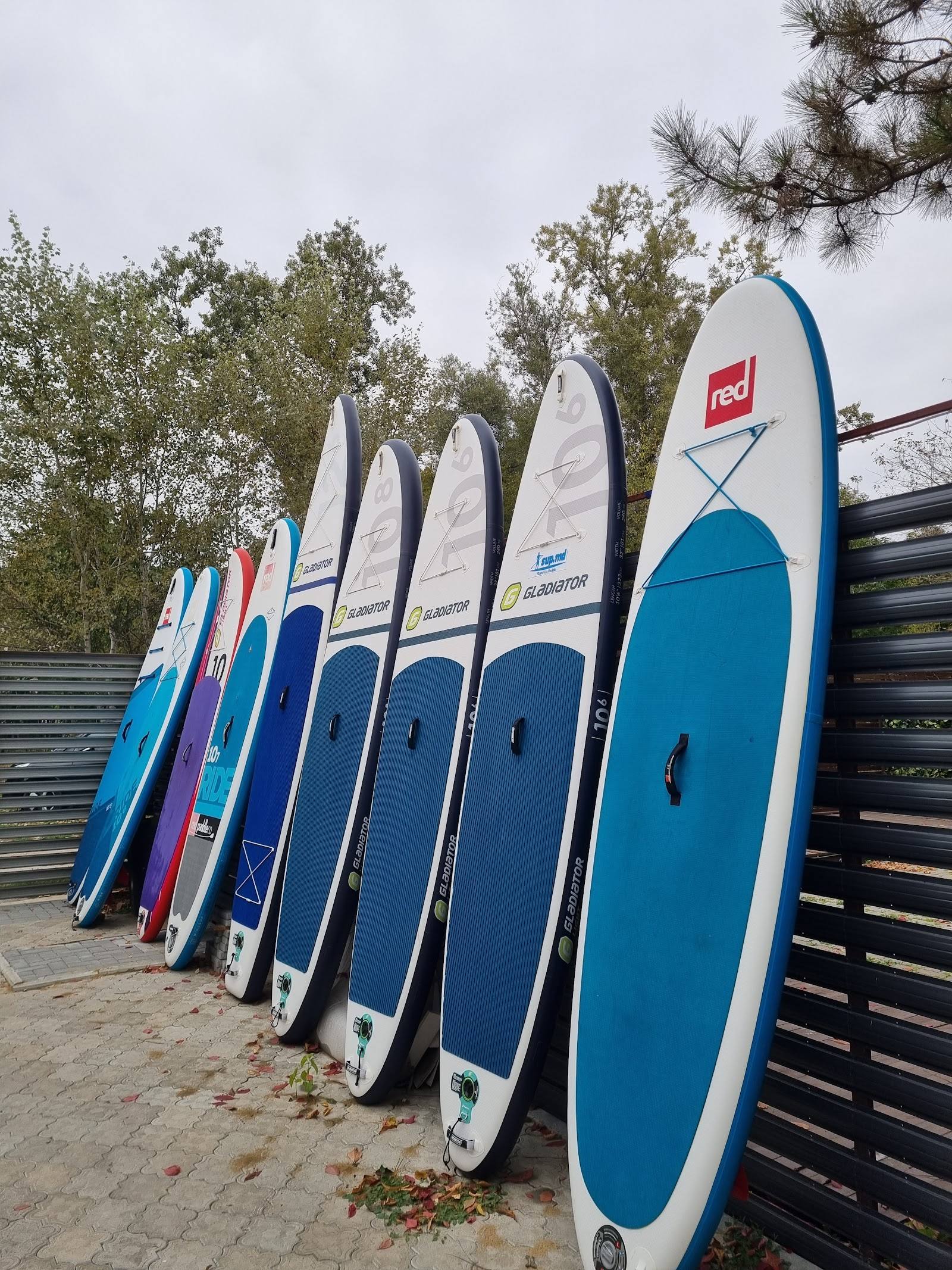 Row of paddleboards and surfboards displayed along outdoor fence