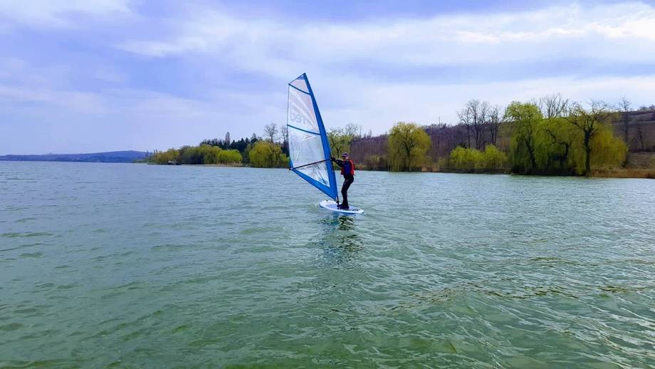 Windsurfing on a calm lake with tree-lined shoreline