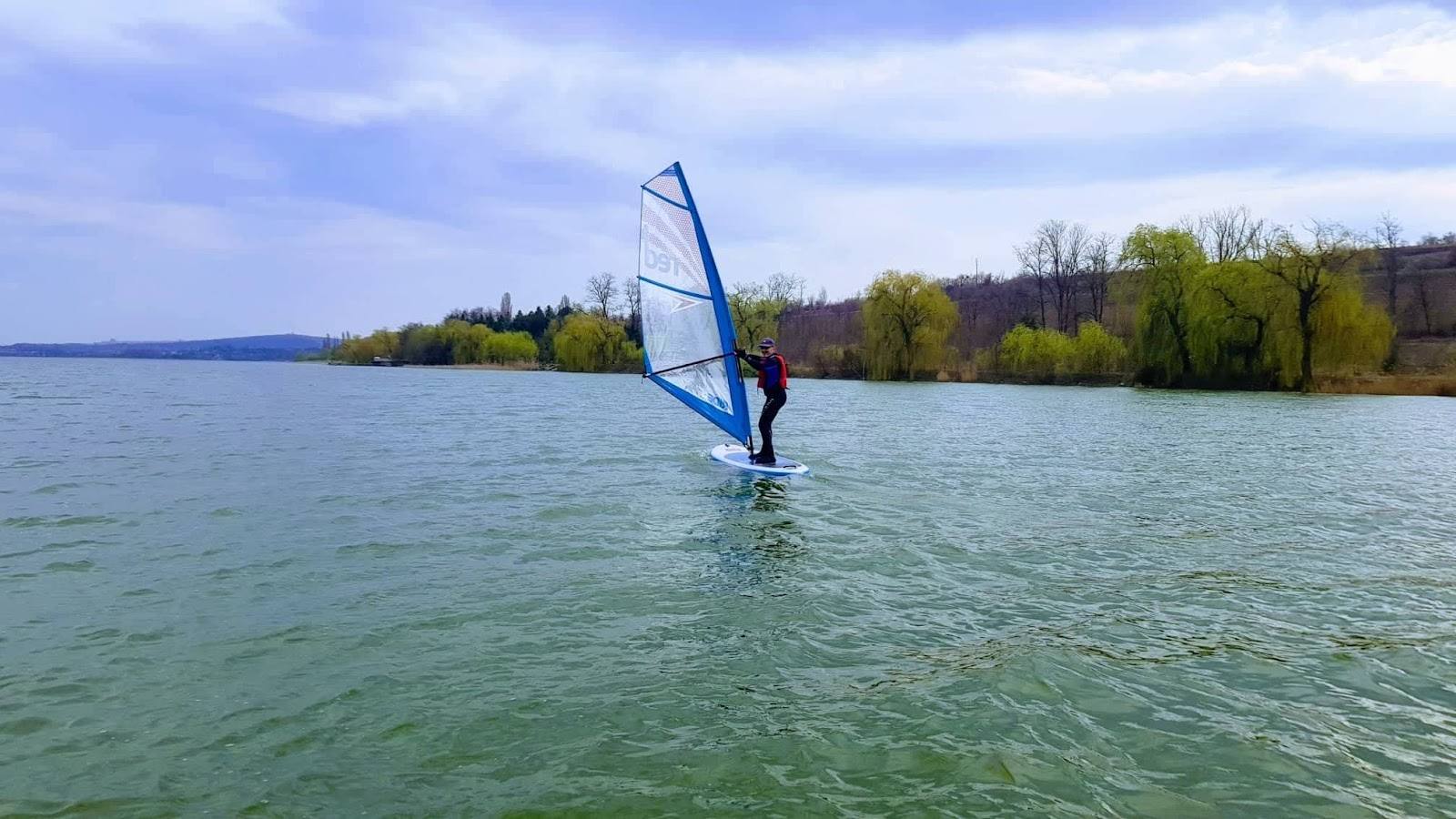Windsurfing on a calm lake with tree-lined shoreline
