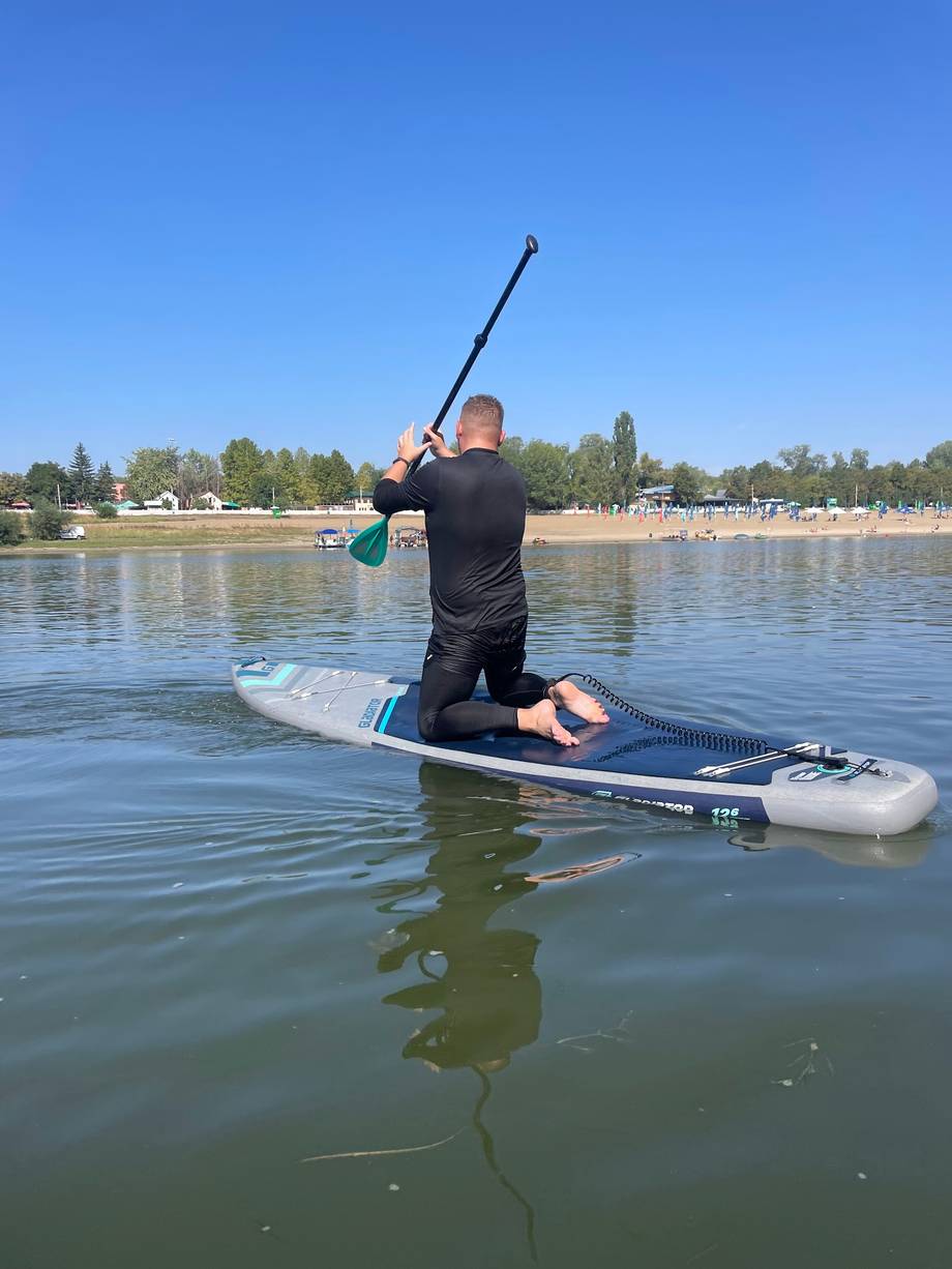 Paddleboarder on a calm river with beach and waterfront trees in the background