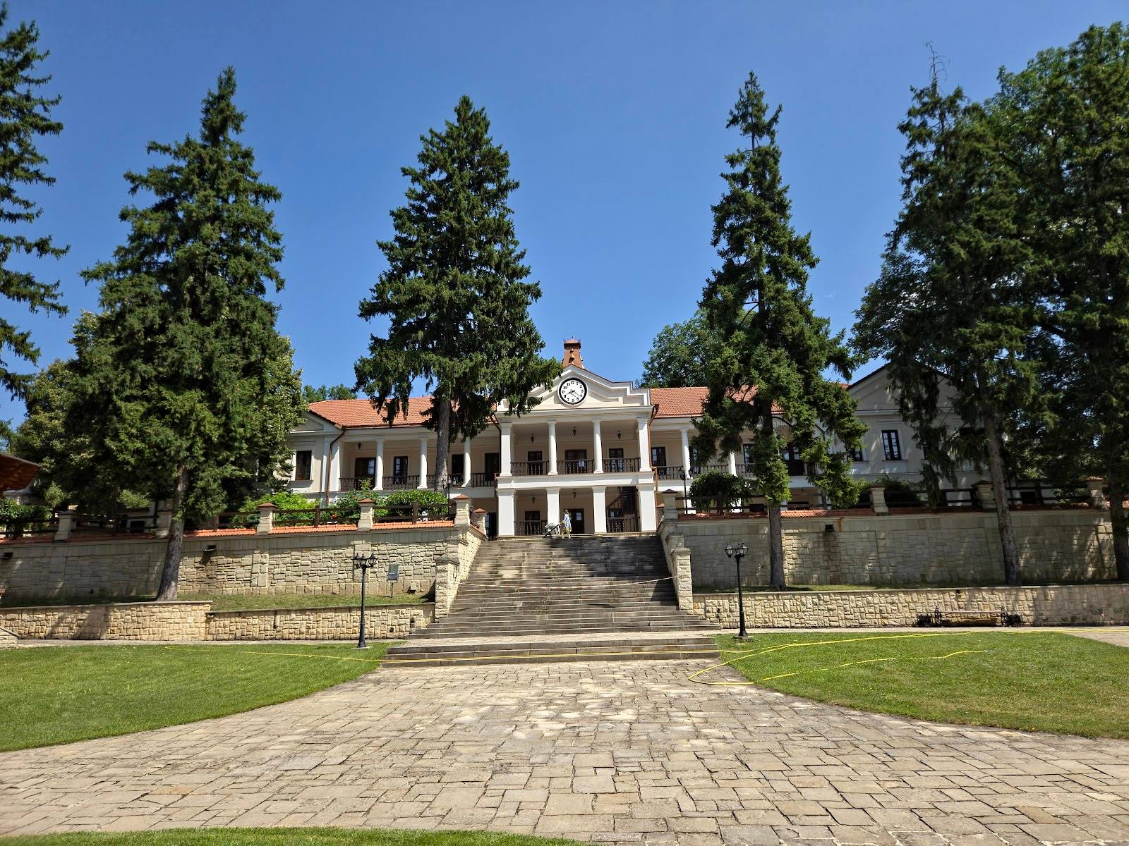 Grand historic mansion with columned entrance and manicured grounds framed by tall evergreens